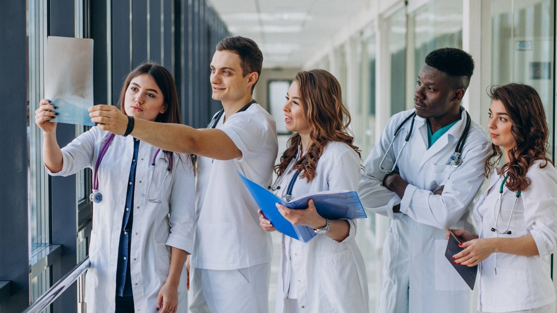 USMLE Clinical Prep – Dr. Heba Tutoring Group of diverse medical students in white coats discussing clinical cases in a hospital corridor — representing Dr. Heba's USMLE prep and clinical skills support.